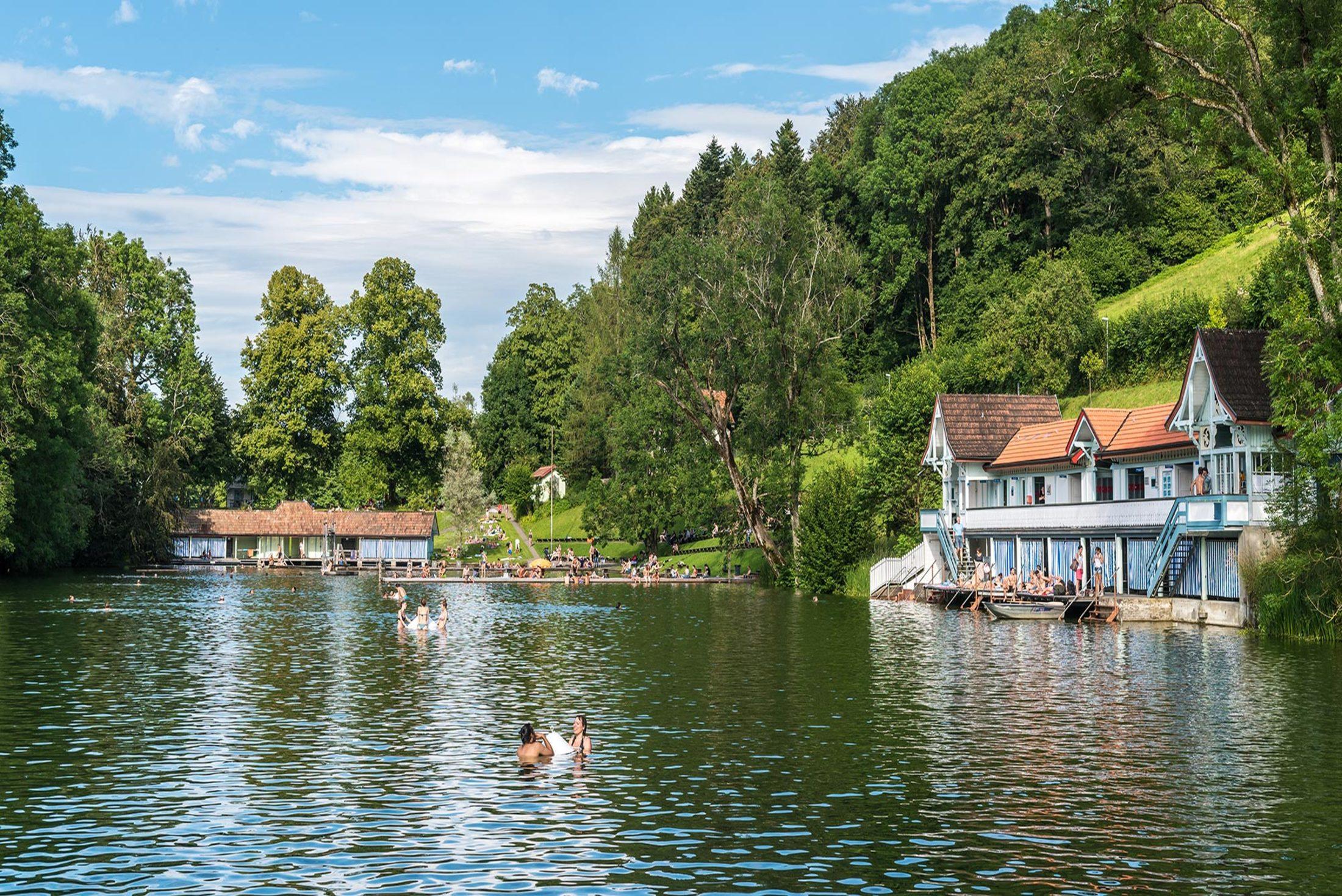 Badesee mit Bäumen und Gebäuden.