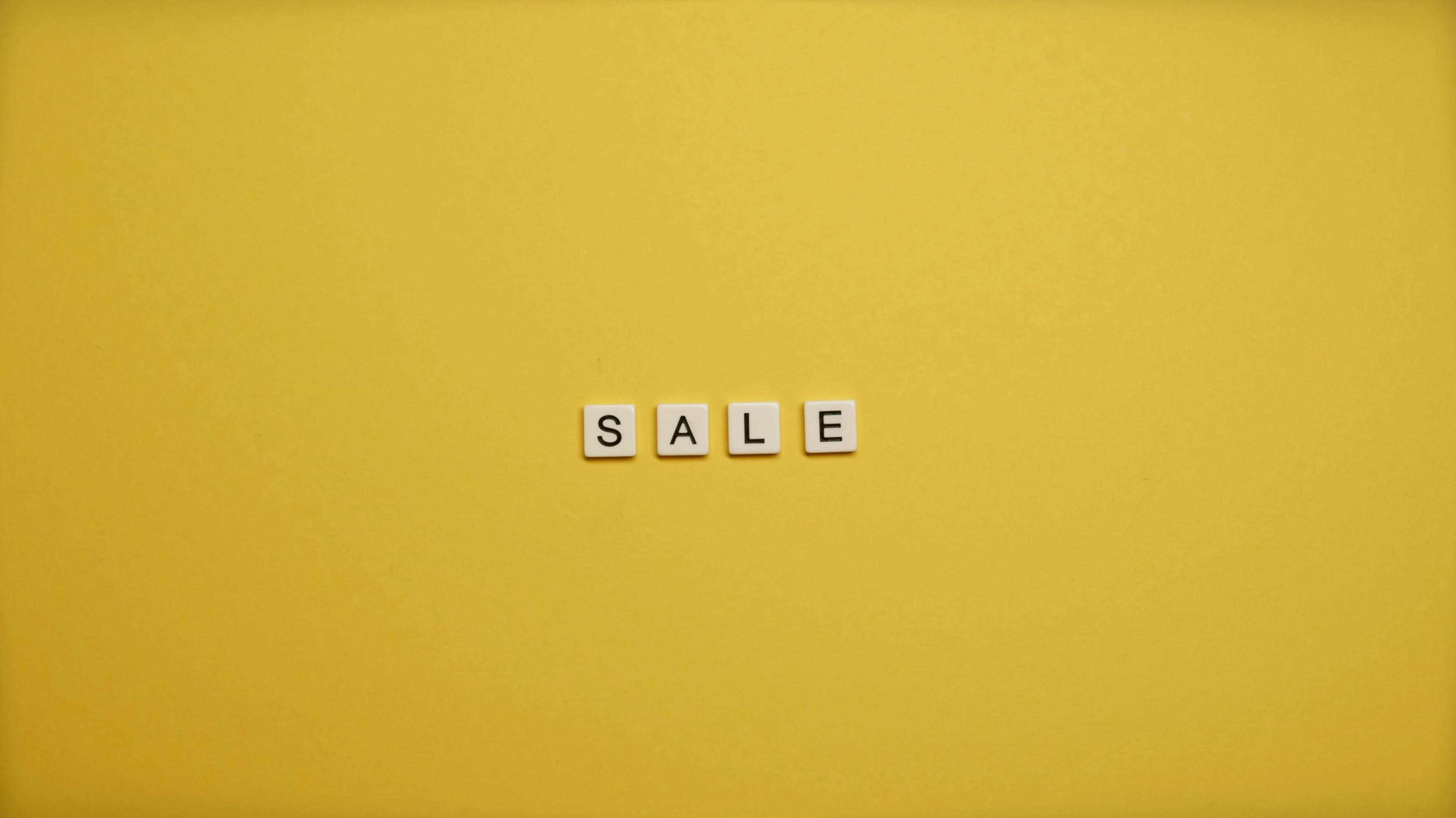 Four white letter stones with the inscription “SALE” are centered on a bright yellow background.